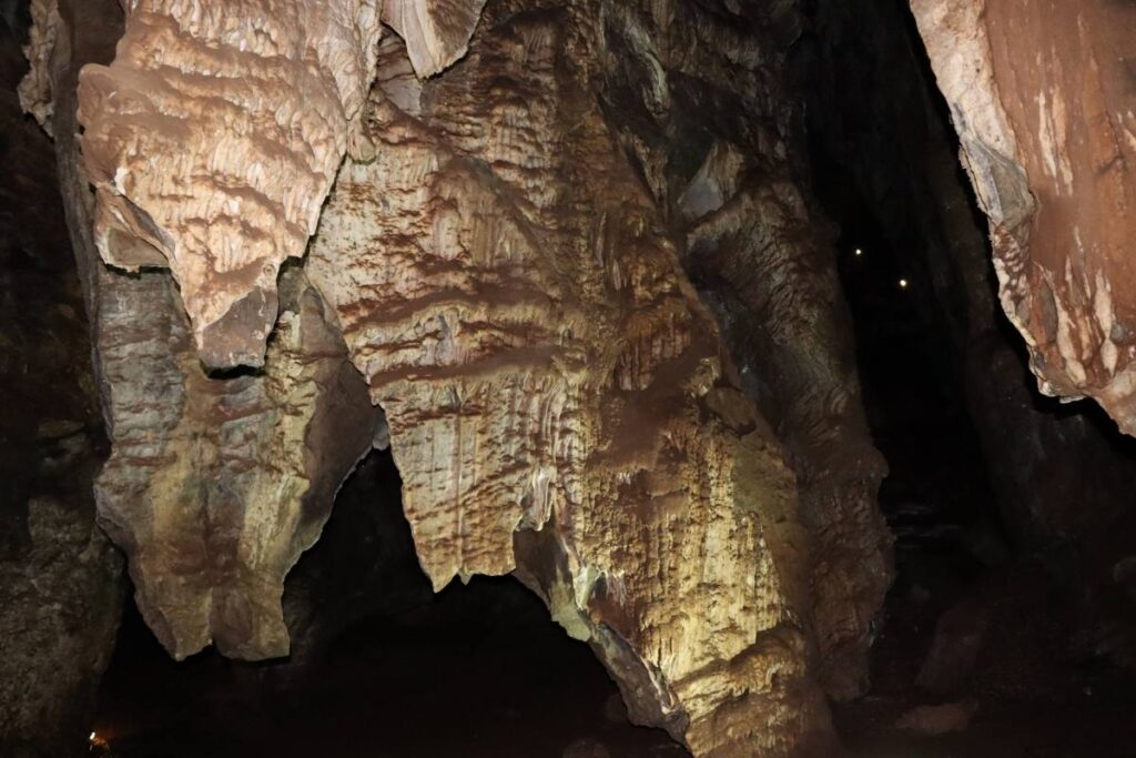 A large, textured limestone formation illuminated inside a dark cave, with jagged edges and layered patterns. As if on a cradle of humankind tour, dim lighting highlights the rugged surface, with hints of darkness in the surrounding area.