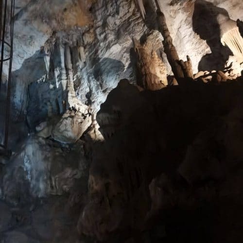 A dimly lit cave interior with rugged rock formations and shadows casting intricate patterns on the textured walls. The light accentuates the natural shapes and contours of the caves surface.