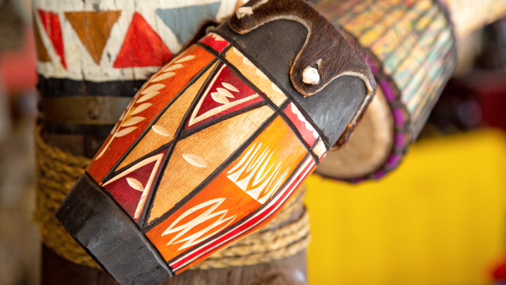 Close-up of an African drum with vibrant geometric patterns in red, orange, and black, reminiscent of the artistry seen on a Lesedi Cultural Village tour. The drum features intricate designs and textures, including small white accents and a patterned rope detail across the body.