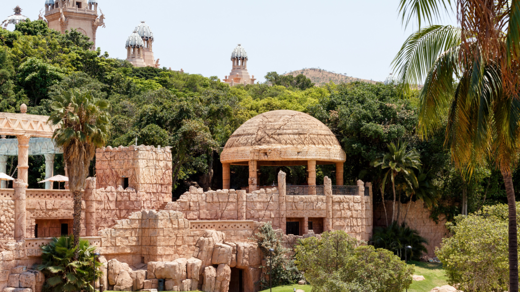 A structure resembling ancient ruins with arches and a large dome, surrounded by lush greenery and palm trees. Tall exotic towers are visible in the background, giving the scene an adventurous and exotic feel.