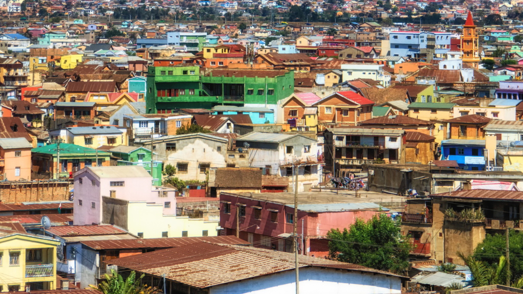 A vibrant cityscape with a dense cluster of colorful houses and buildings. The structures vary in color, including shades of green, pink, orange, and brown, creating a lively and diverse scene. A few trees are scattered throughout the area.