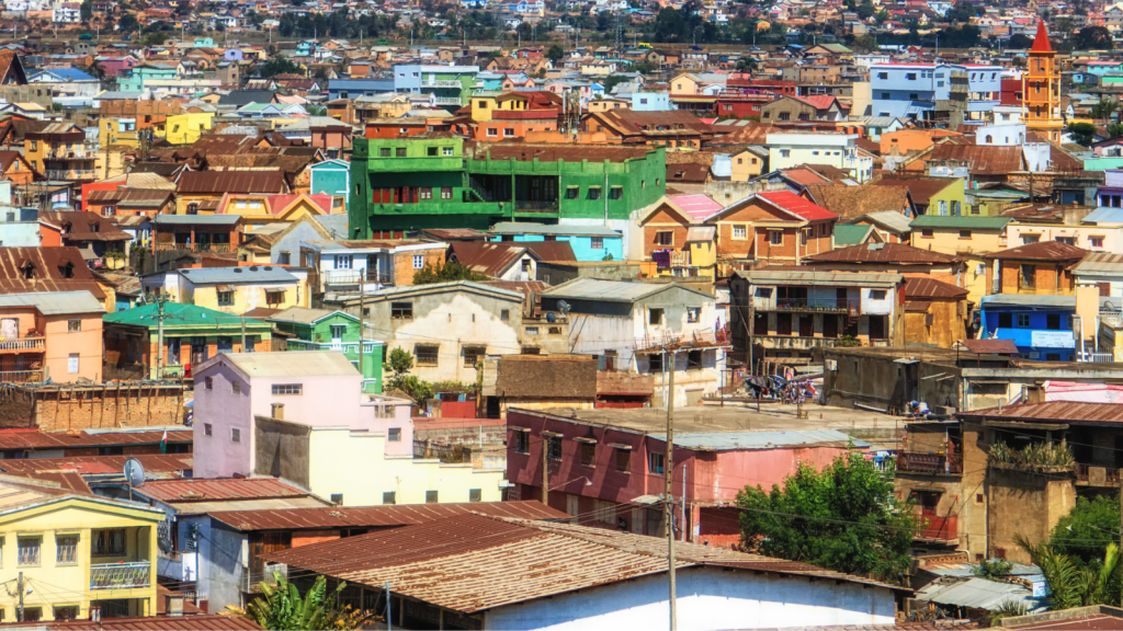 A vibrant and densely packed urban landscape with colorful houses, featuring a bright green building as a focal point. The varied architecture and warm tones showcase a lively, bustling city scene under a clear sky.