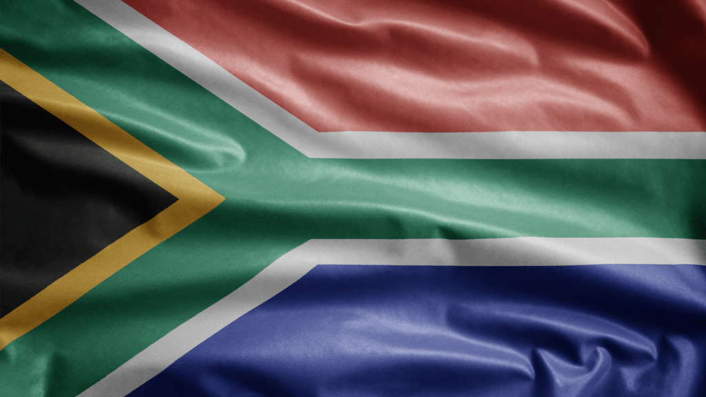 The image shows the flag of South Africa, featuring horizontal bands of red and blue, a green Y-shape with white borders, a black triangle on the hoist side with a yellow border.